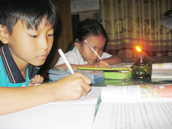 Không có điện, hai đứa con anh Sĩ phải chia nhau chút ánh sáng của ngọn đèn dầu để học bài. Ảnh: D.C.H