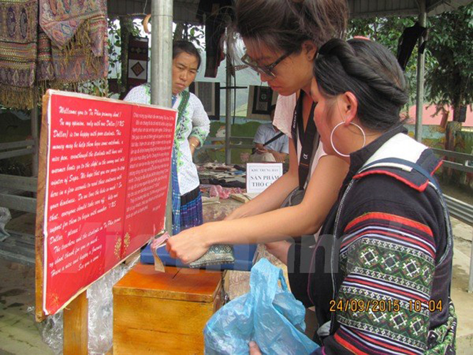 Chị Thò Thị Sông đang hướng dẫn du khách trả tiền vào thùng và ghi lại cảm nhận về trường. (Ảnh: PM/Vietnam+)
