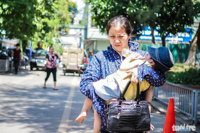  Một người phụ nữ bế một đứa trẻ di chuyển vội vã trong nắng nóng - Ảnh: Nguyễn Khánh