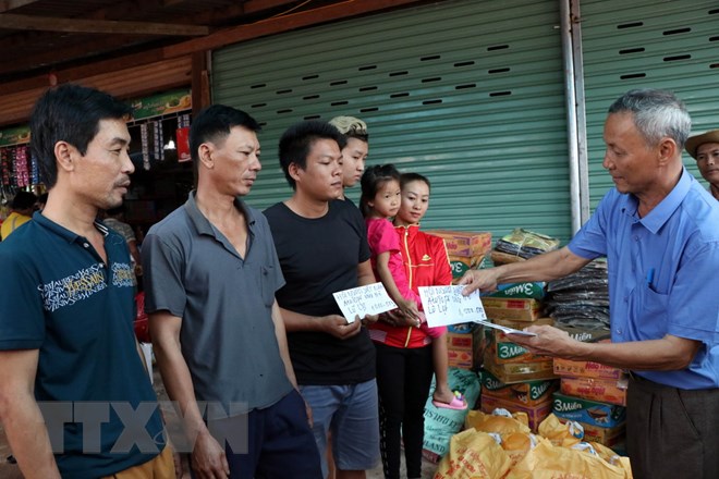 Chủ tịch Hội người Việt Nam tại tỉnh Attapeu Võ Văn Mừng trao tặng số tiền 1 triệu Kip cho 3 gia đình bị ảnh hưởng sau sự cố vỡ đập thủy điện. (Ảnh: Quang Thái/TTXVN)