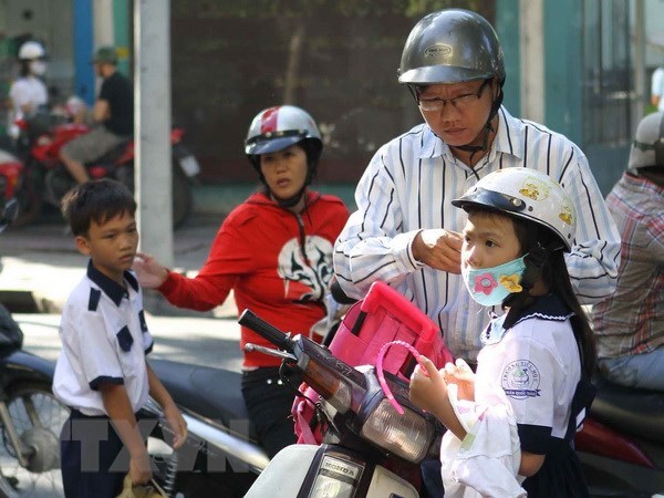 Phụ huynh đội mũ bảo hiểm cho trẻ khi tham gia giao thông. (Ảnh: TTXVN)