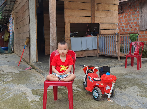 Cháu Hoàng Minh Tuấn ngồi trước ngôi nhà của hai mẹ con.