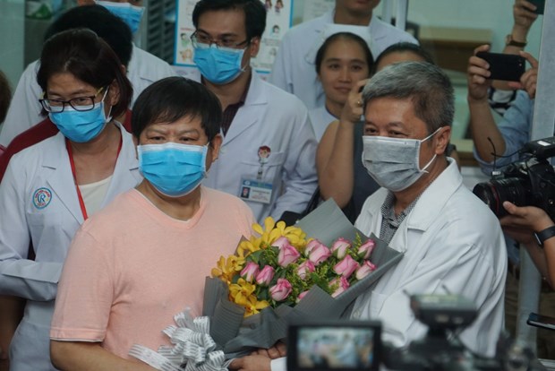   Thứ trưởng Bộ Y tế Nguyễn Trường Sơn (bên phải) tặng hoa cho bệnh nhân Li Ding trong vòng vây. Ảnh: Đinh Hằng – TTXVN