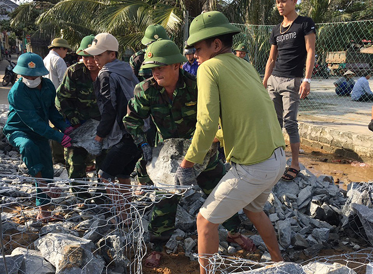 cán bộ chiến sĩ biên phòng cùng nhân dân địa phương gia cố kè chắn sóng biển bị sạt sau 2 trận lũ.