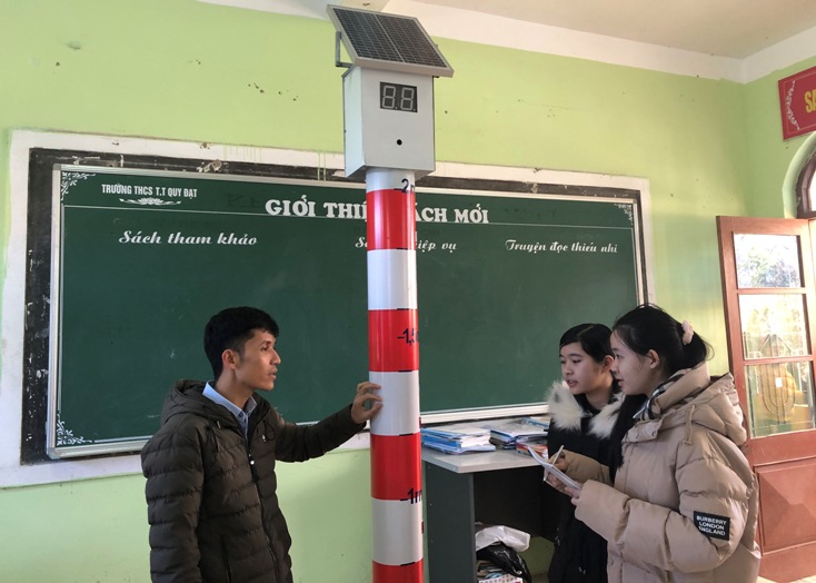 Hai học sinh Nguyễn Khánh Trang và Đào Hoàng Quỳnh Như cùng thảo luận với thầy giáo về thiết bị cảnh báo mực nước thông minh.