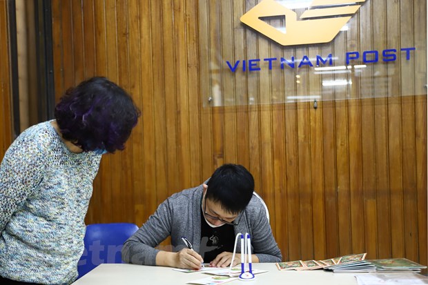  Họa sĩ Nguyễn Quang Vinh ký tặng người đến mua tem. (Ảnh: Hoài Nam/Vietnam+)