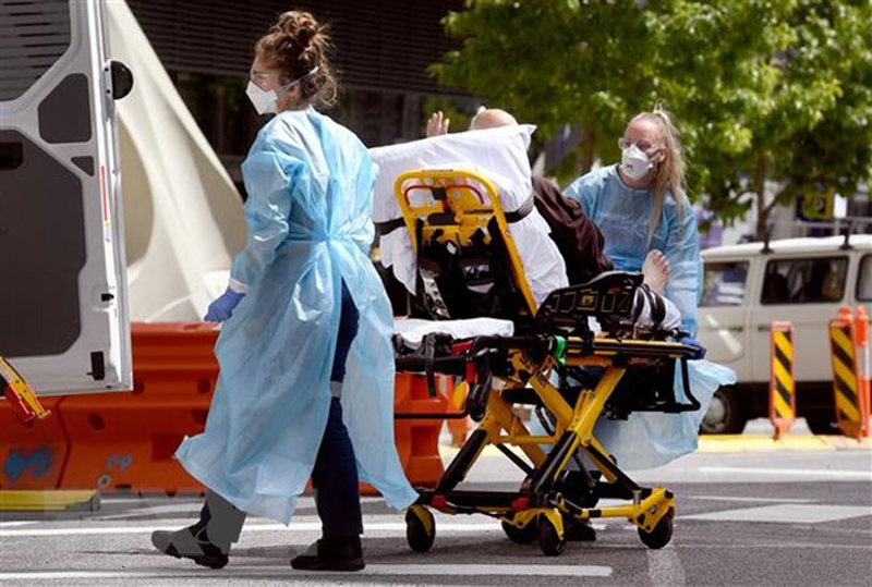 Nhân viên y tế chuyển bệnh nhân COVID-19 tới bệnh viện tại Melbourne, Australia. (Ảnh: AFP/TTXVN)