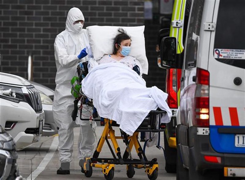 Nhân viên y tế chuyển bệnh nhân COVID-19 lên xe cứu thương tại thành phố Melbourne, Australia. (Ảnh: AFP/TTXVN)