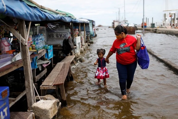 Một người mẹ cùng con gái đi qua vùng nước ngập do nước biển dâng taị phía Bắc Jakarta, Indonesia năm 2020. Ảnh: Reuters