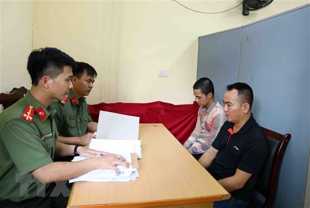 Lực lượng chức năng lấy lời khai bị can Nguyễn Quang D (áo đen) và bị can Đinh Tiến S (áo kẻ). (Ảnh: Phạm Kiên/TTXVN)