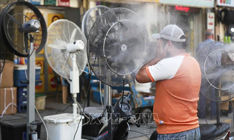 Người dân dùng quạt phun sương để tránh nóng tại Baghdad, Iraq, ngày 23/7/2023. Ảnh: AFP/TTXVN