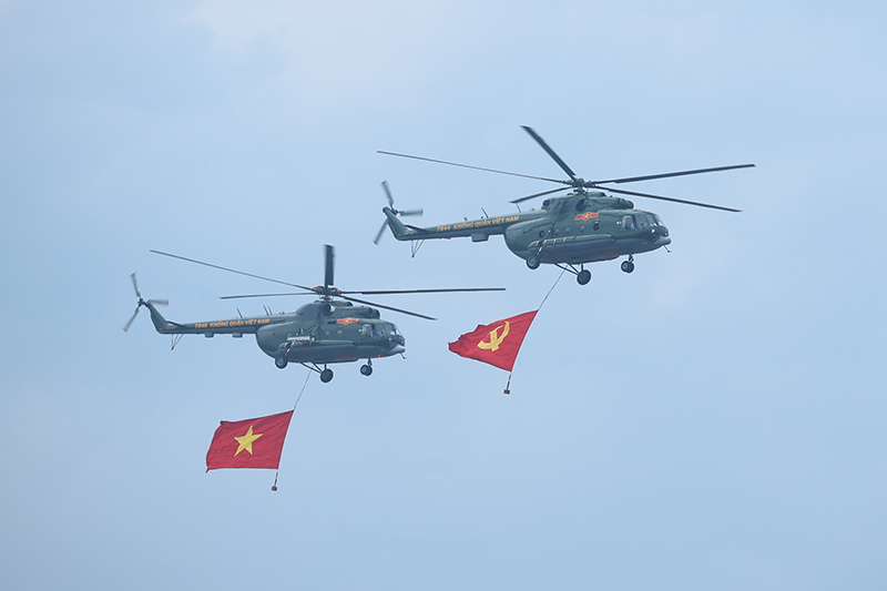 Các biên đội trực thăng vũ trang thuộc Quân chủng Phòng không-Không quân, Quân đội nhân dân Việt Nam mang theo cờ Đảng, cờ Tổ quốc Việt Nam diễu hành tiến qua sân vận động Điện Biên. Ảnh: VGP/Nhật Bắc